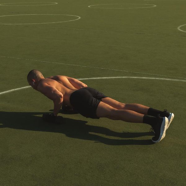 Man doing push-ups with perfect form on a dark floor.